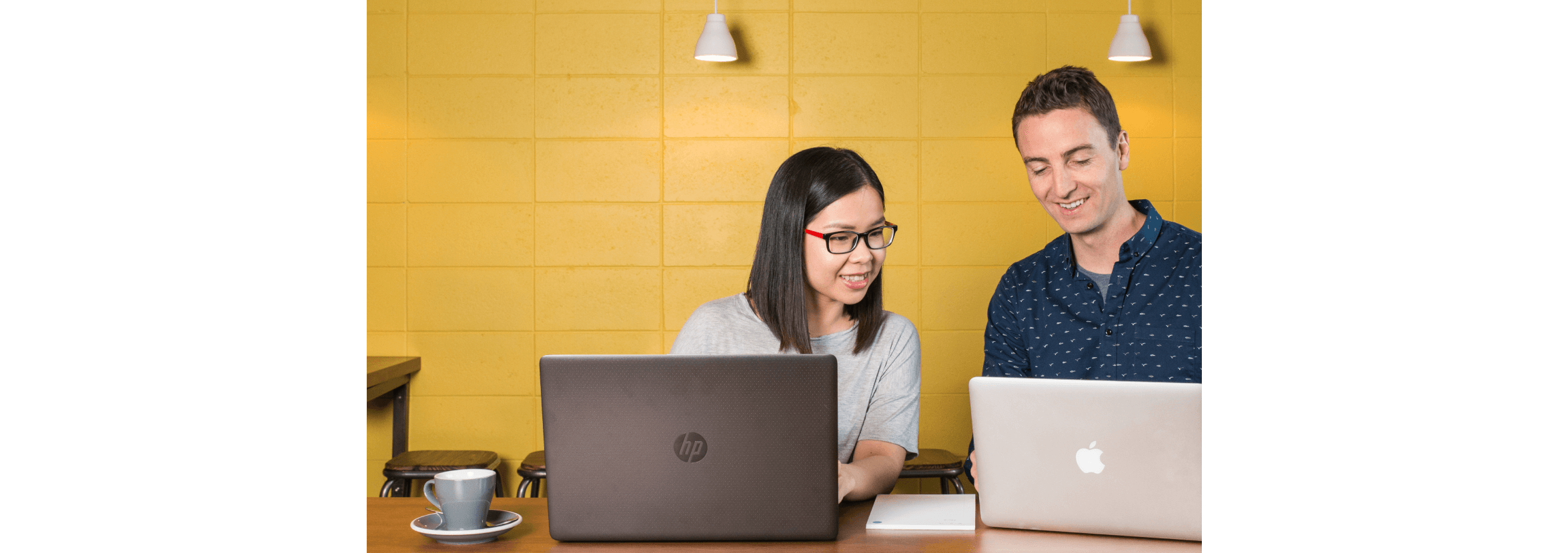 Two people working together at their laptops in an office kitchen.