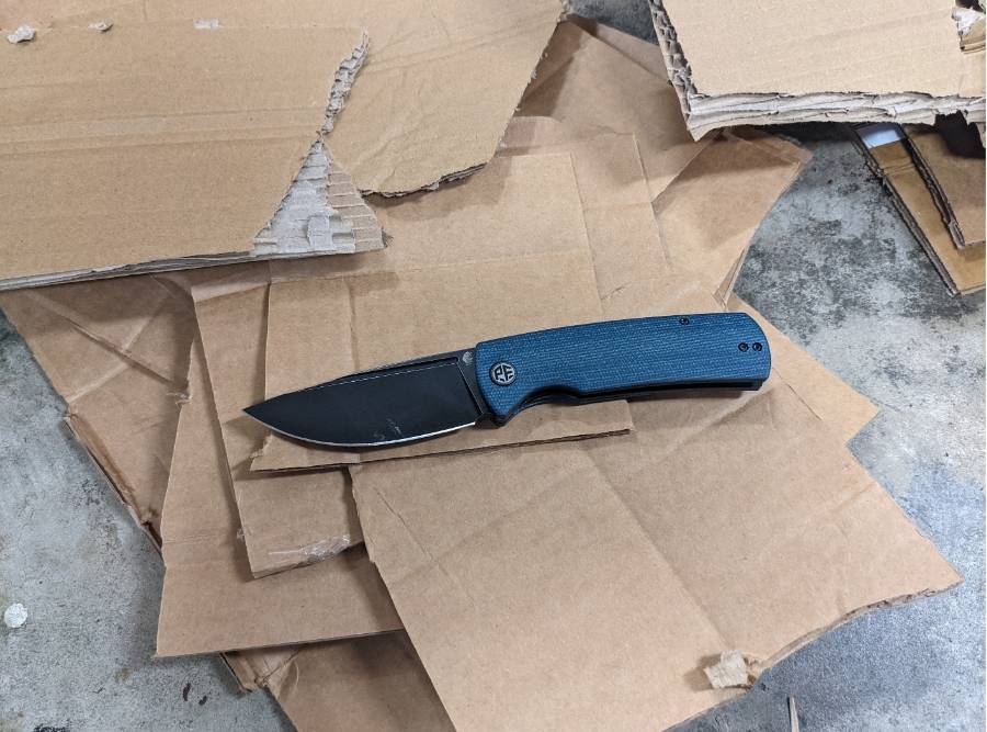 Petrified Fish Beluga PFP01 folding knife with blue handle and black blade cutting cardboard in real-world EDC test.